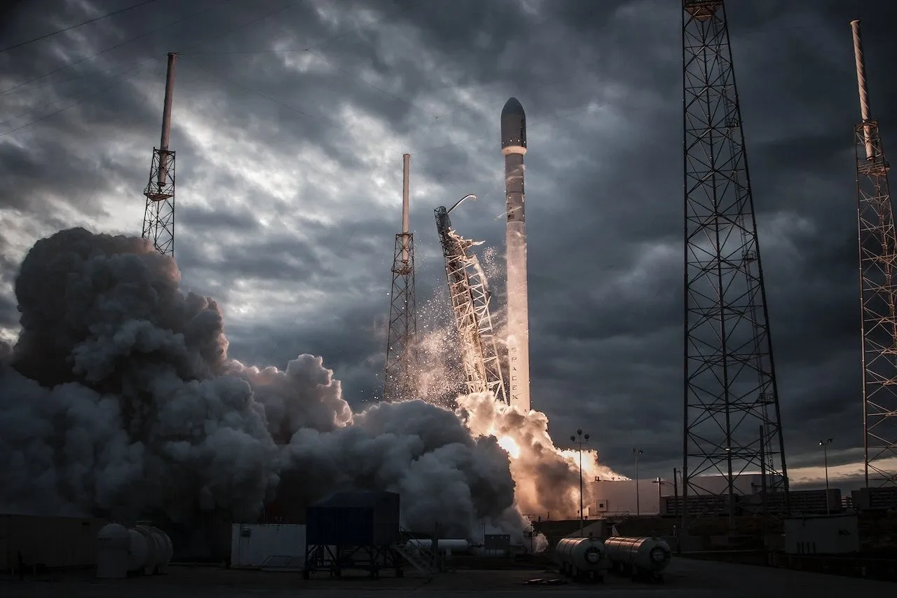 A rocket on its launch pad surrounded by smoke and dark clouds after a failed launch.