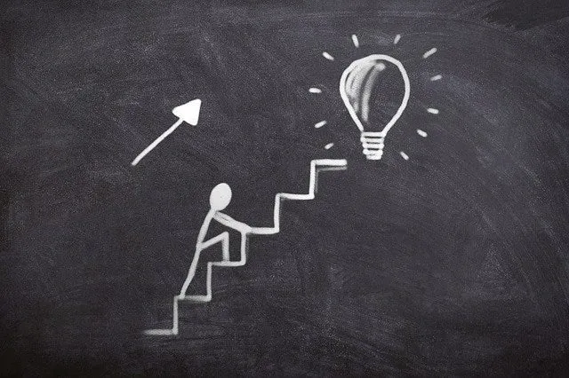 A chalk drawing of a figure climbing stairs toward a lightbulb.