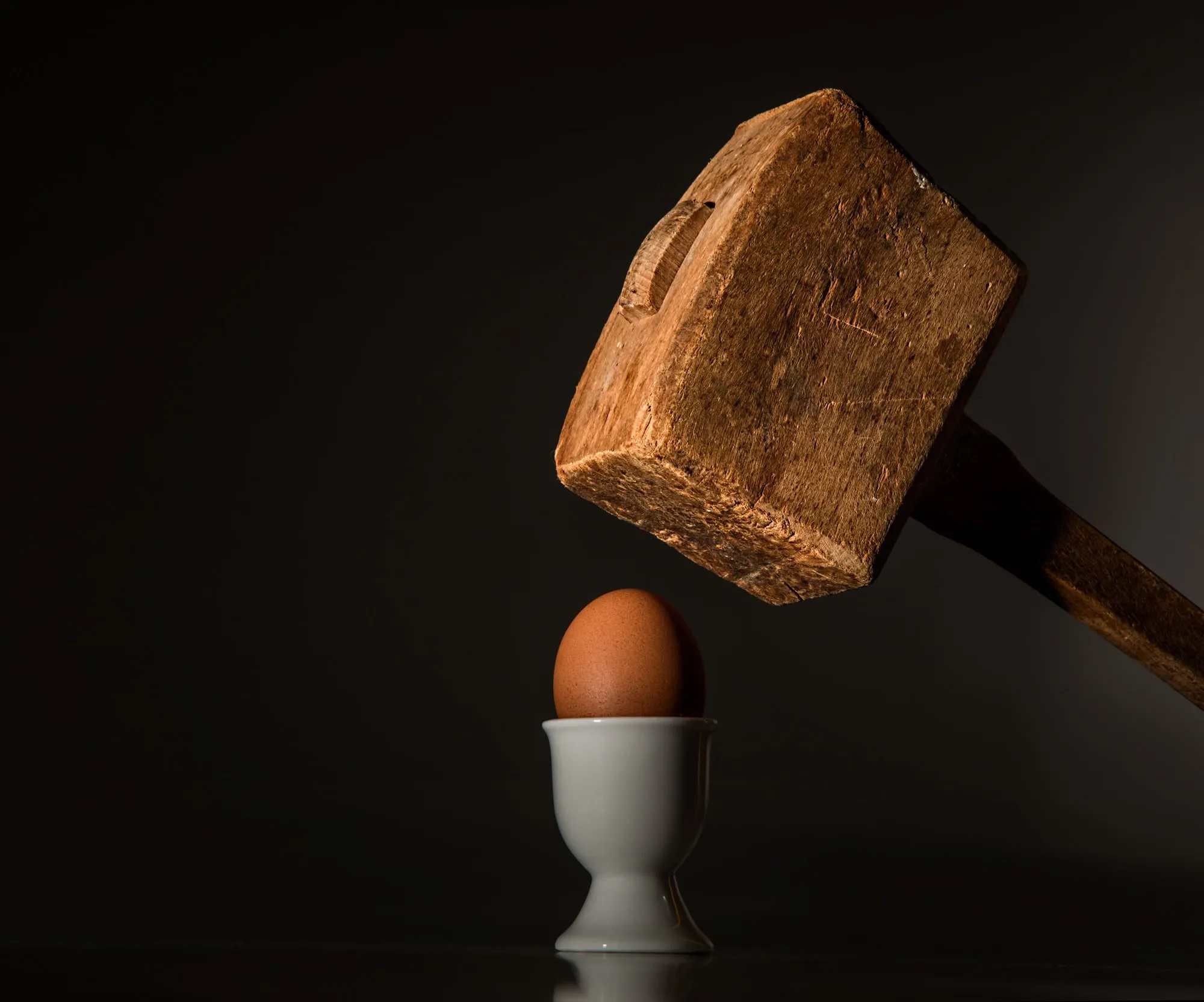 A wooden mallet poised above an egg in an egg cup.
