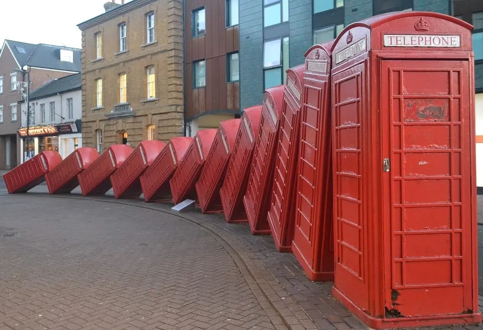 A row of red telephone boxes toppled over like dominoes on a street.