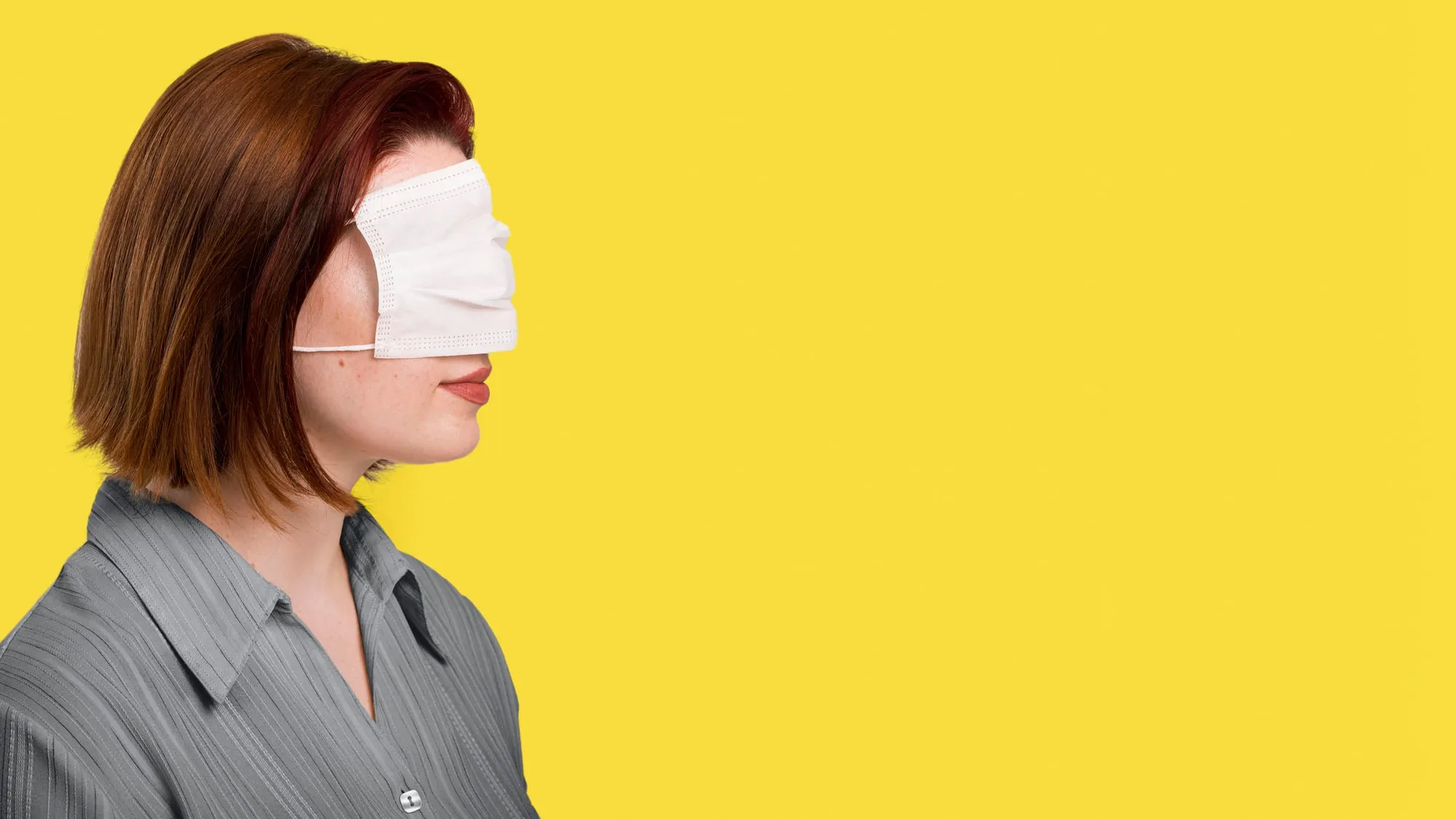 A woman in a grey shirt wearing a white blindfold against a yellow background.