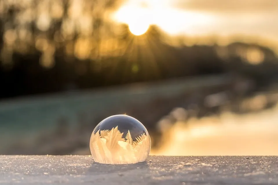 A frozen bubble with ice crystals resting on snow at sunset.