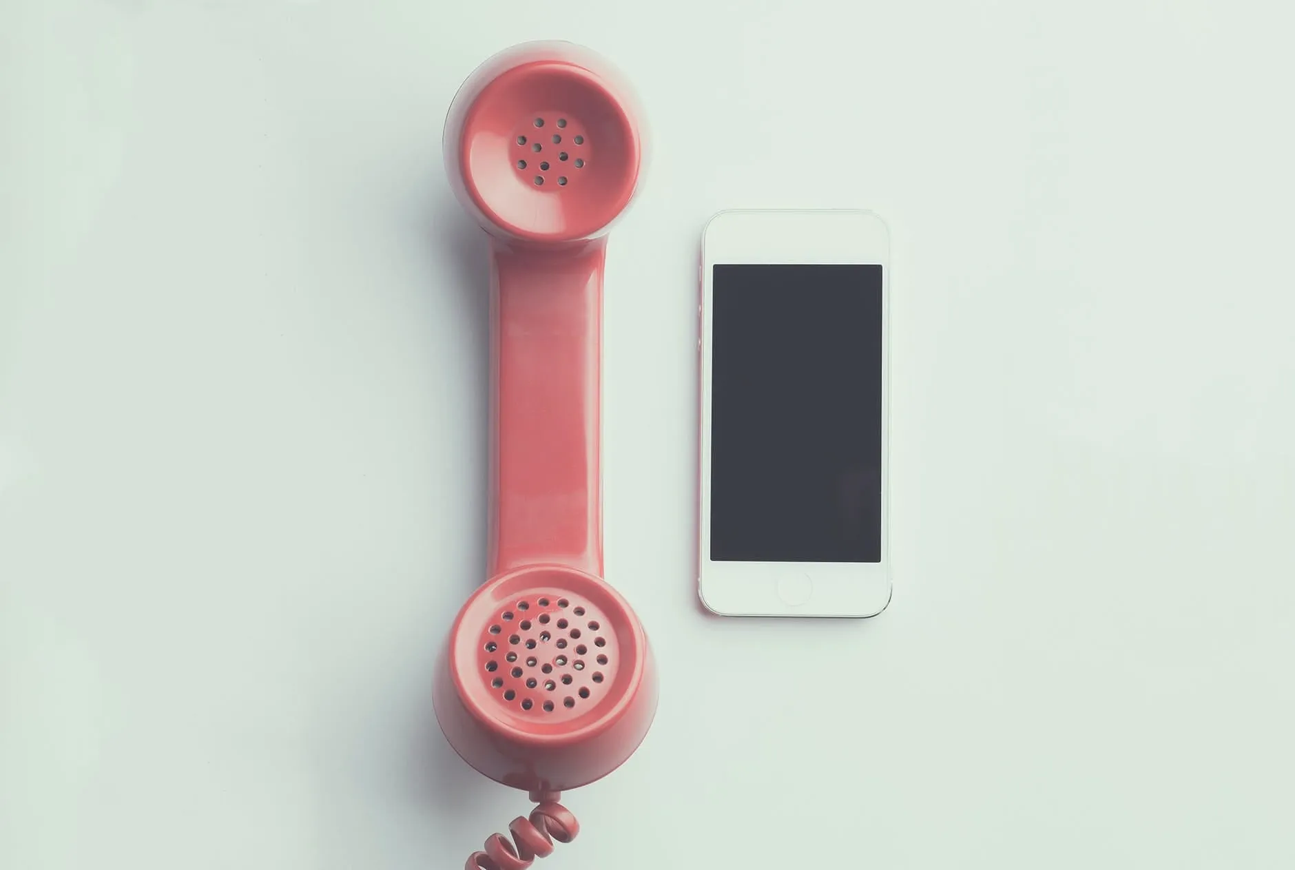 A red retro telephone handset beside a smartphone on a white surface.