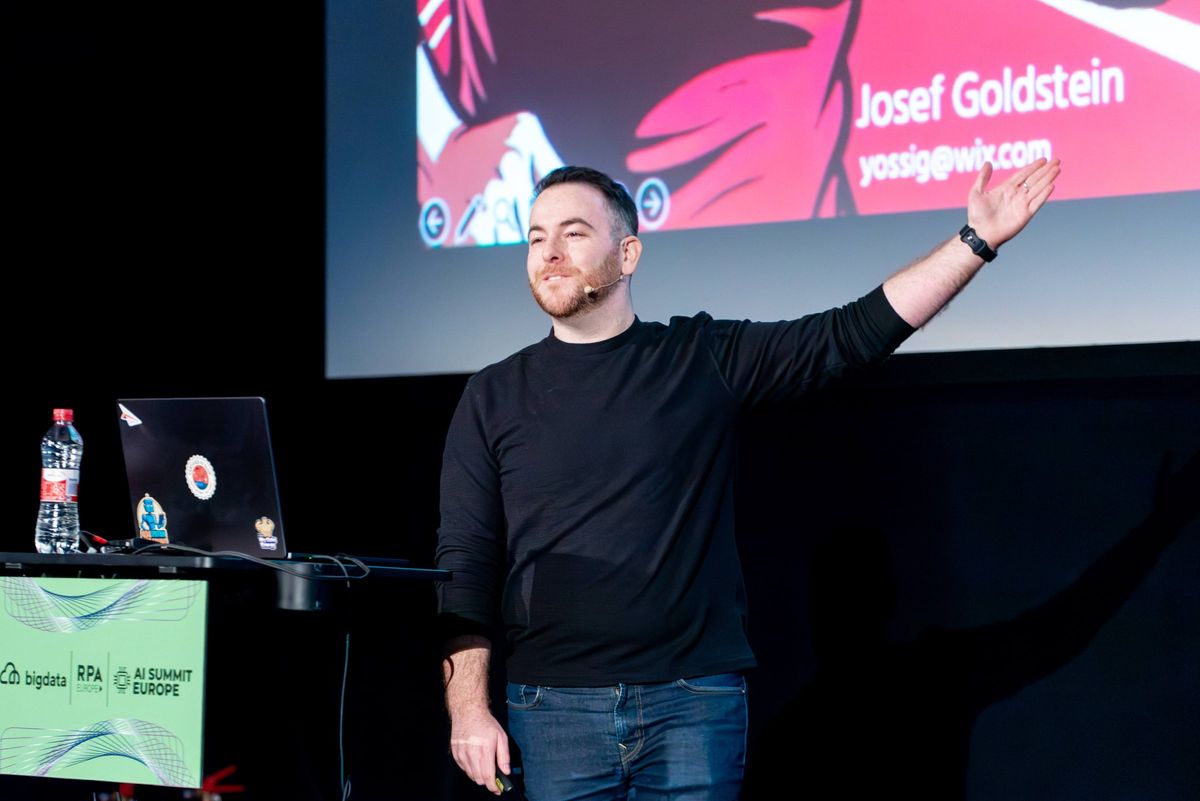 Yossi on stage at AI Summit Europe, arms wide, title slide behind him